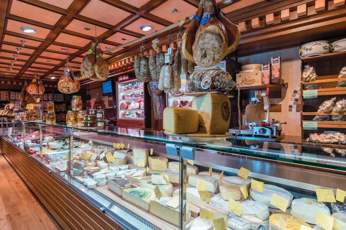 Banco della gastronomia Zanini con prosciutti appesi e vetrina dei formaggi